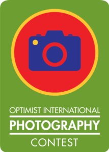 A green background, at the top is a cartoon image of a camera. At the bottom it says "Optimist International Photography Contest"